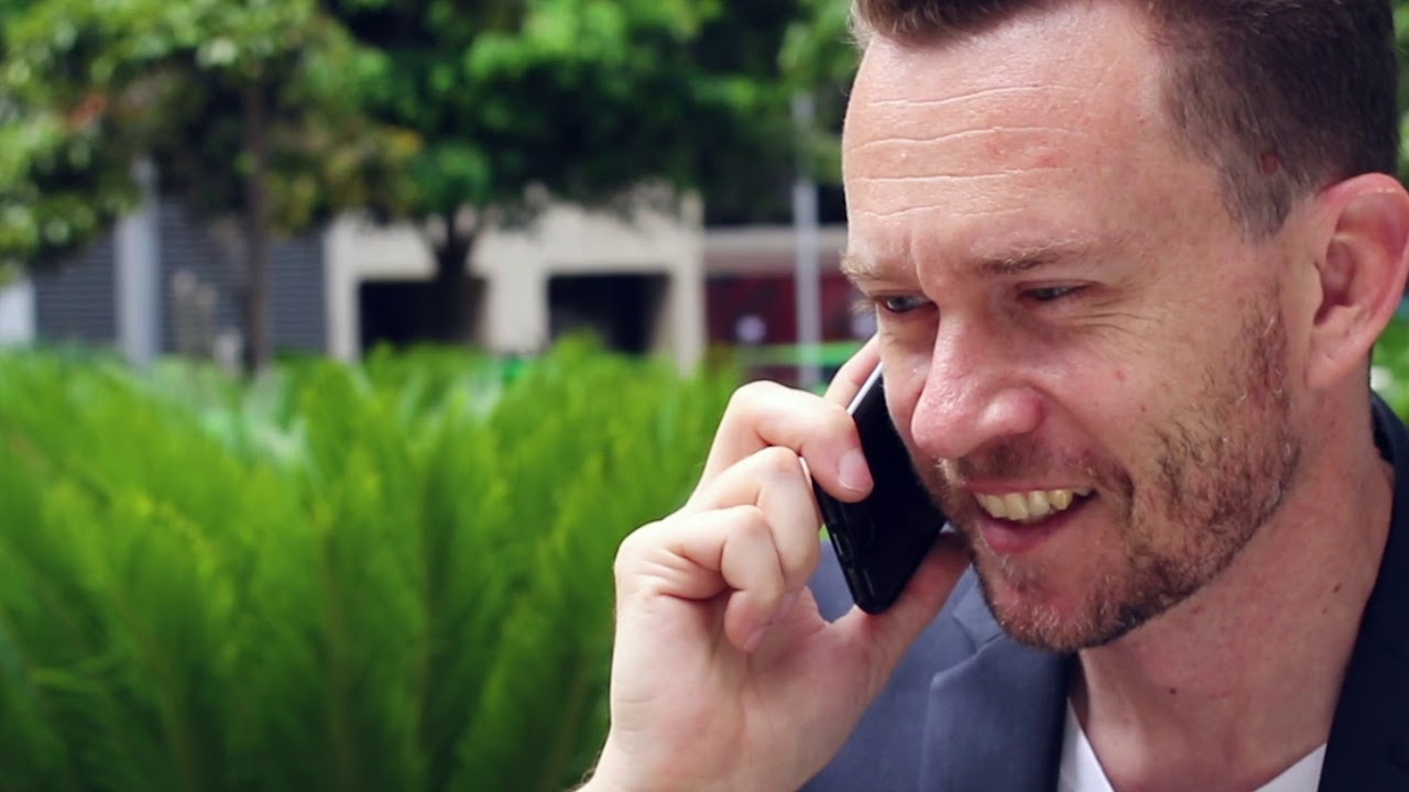 A man smiling while talking someone on the phone